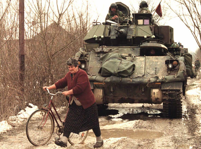 Bosnialainen serbinainen pujottelee Naton amerikkalaisten ”rauhanturvajoukkojen” panssarivaunujen välissä. Kuva otettu Pelagićevon lähellä serbien hallitsemalla alueella pohjoisessa Bosniassa tammikuussa 1996.